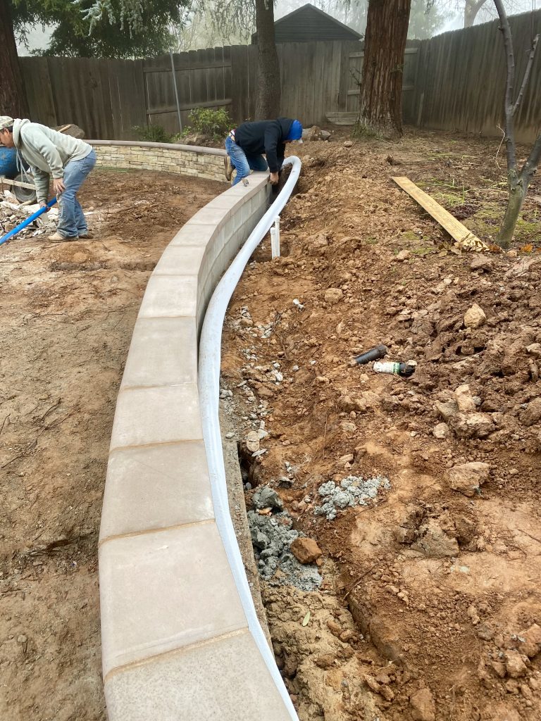 Drainage pipe installation behind the CMU retaining wall in the Wedemeyer backyard to collect groundwater and protect the wall from hydrostatic pressure.