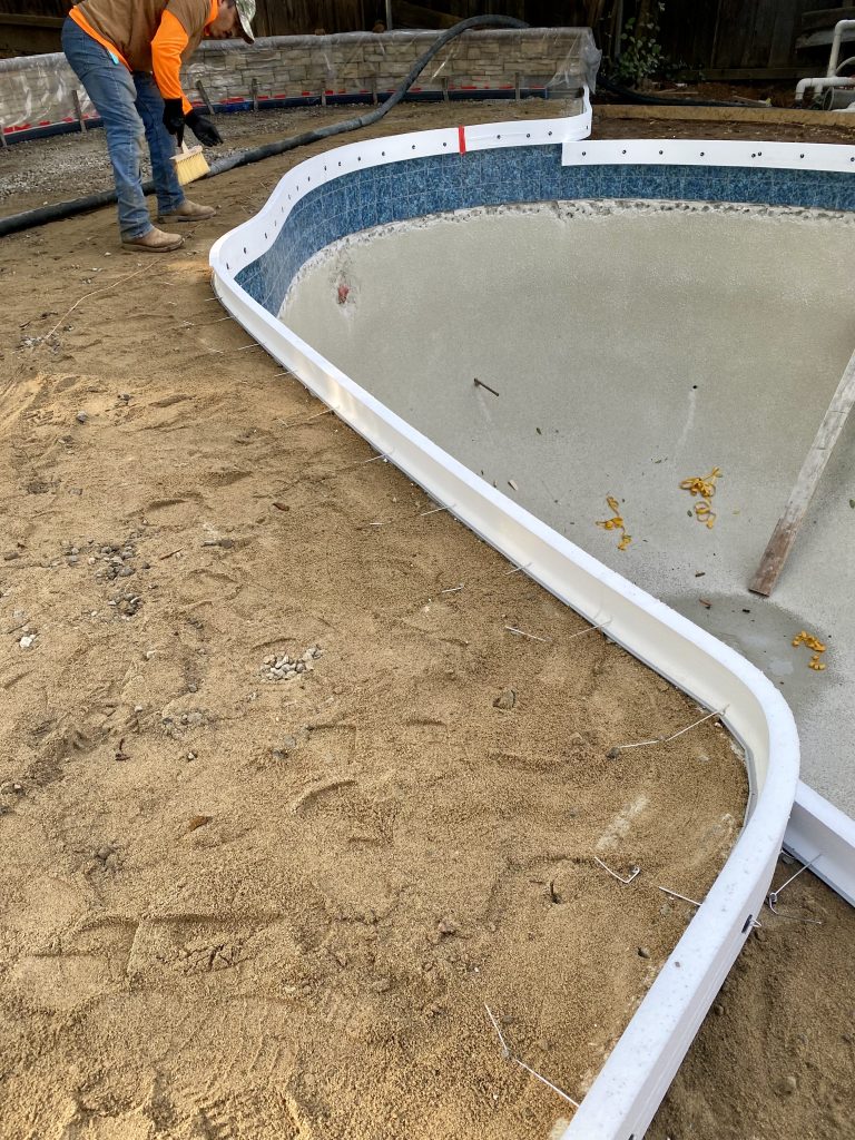 Pool coping installation showing the sand setting bed and raised pool wall elevation designed to protect the pool deck from erosion and improve long-term performance in the Wedemeyer backyard renovation.