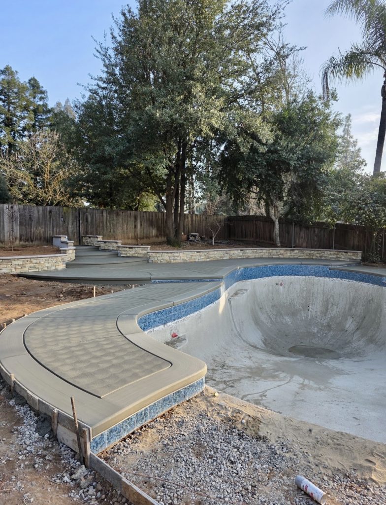 Completed concrete pool deck featuring a smooth border, decorative sweat finish, and matching bullnose coping around the pool and stairways during the Wedemeyer backyard renovation by Sunset Construction.