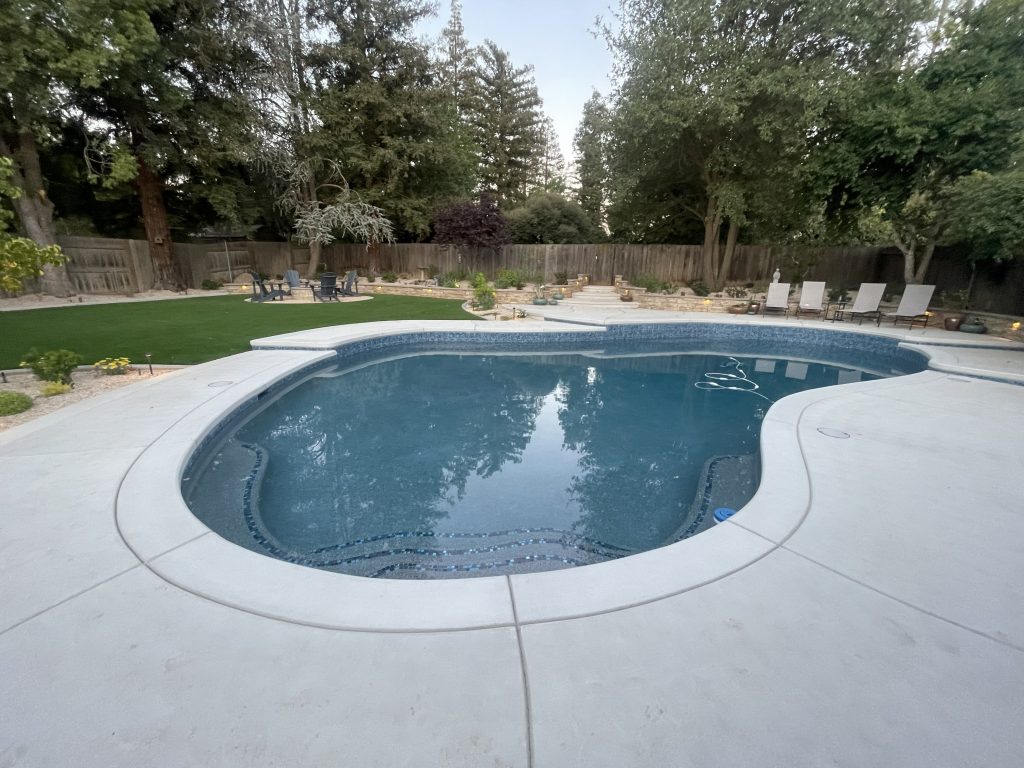 Completed Wedemeyer backyard renovation featuring decorative retaining walls, expanded pool deck, architectural stairways, custom fire pit gathering area, and integrated outdoor living spaces by Sunset Construction.