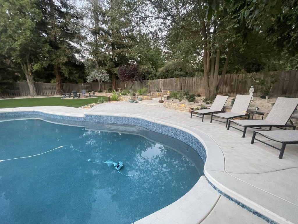 Completed pool deck, architectural retaining walls, illuminated stairways, and custom outdoor living spaces in the finished Wedemeyer backyard renovation by Sunset Construction.