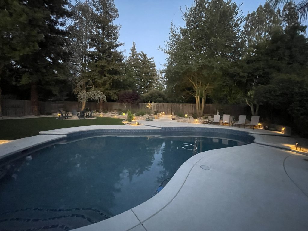 Evening view of the completed Wedemeyer backyard renovation featuring illuminated retaining walls, architectural stairways, expanded pool deck, and landscape lighting by Sunset Construction.