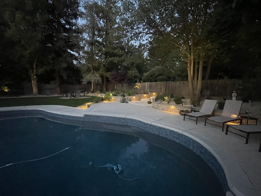 Landscape lighting highlighting the decorative retaining walls, stairways, expanded pool deck, and poolside seating area in the completed Wedemeyer backyard renovation.