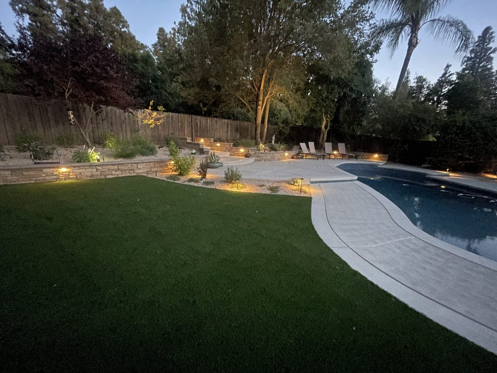 Final evening view of the completed Wedemeyer backyard renovation featuring illuminated retaining walls, expanded pool deck, architectural stairways, and custom outdoor living spaces by Sunset Construction.